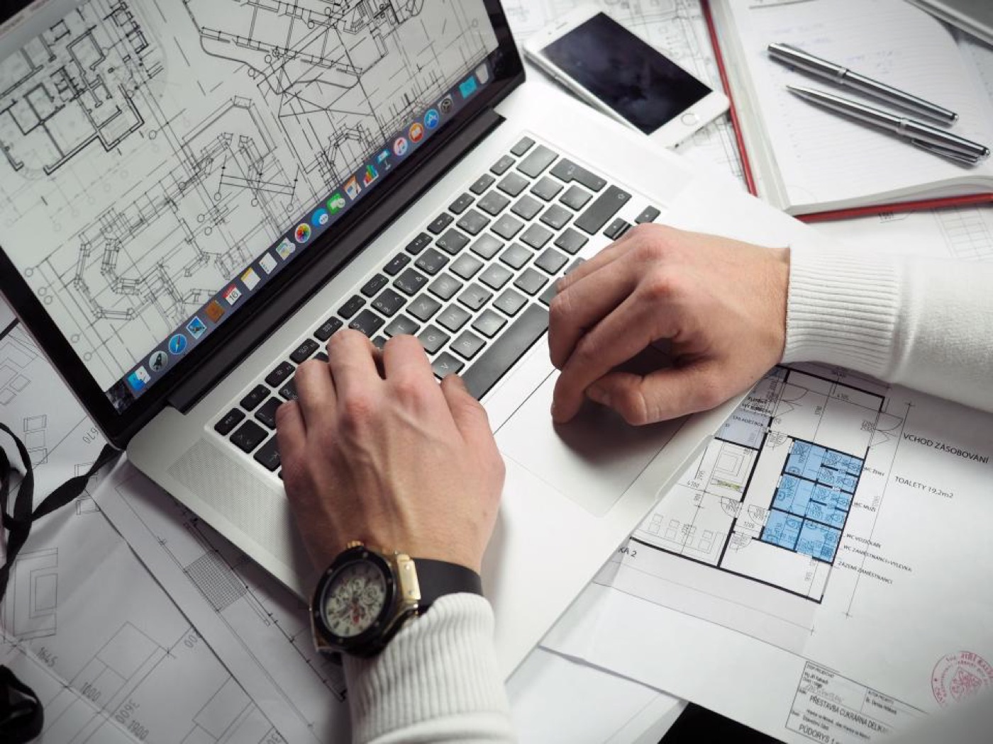 Hands on a laptop keyboard next to page layout sketches